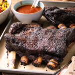 A baking sheet containing smoked beef ribs and bbq sauce.