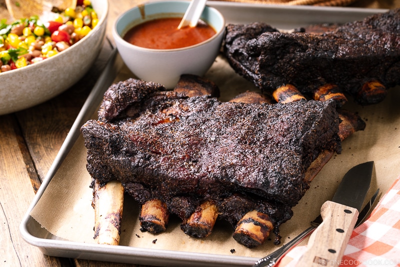 A baking sheet containing smoked beef ribs and bbq sauce.