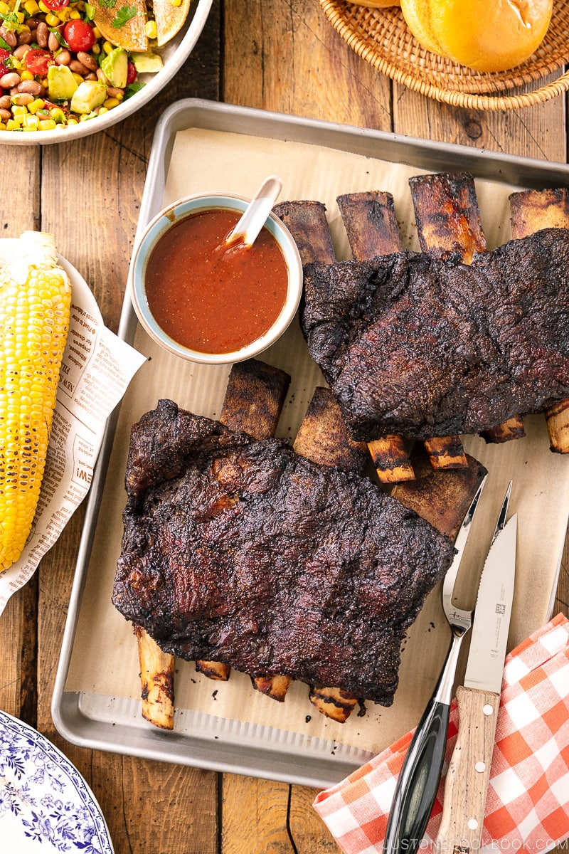 A baking sheet containing smoked beef ribs and bbq sauce.