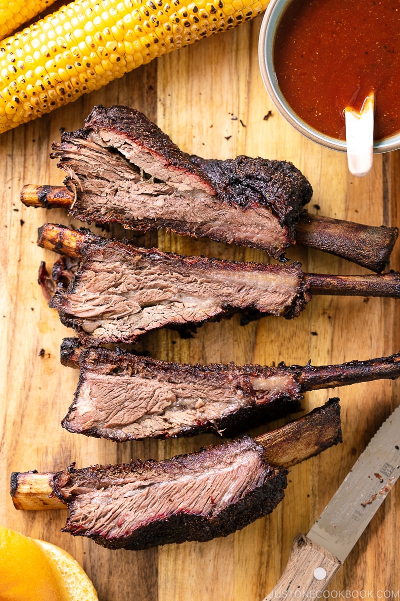 A baking sheet containing smoked beef ribs and bbq sauce.