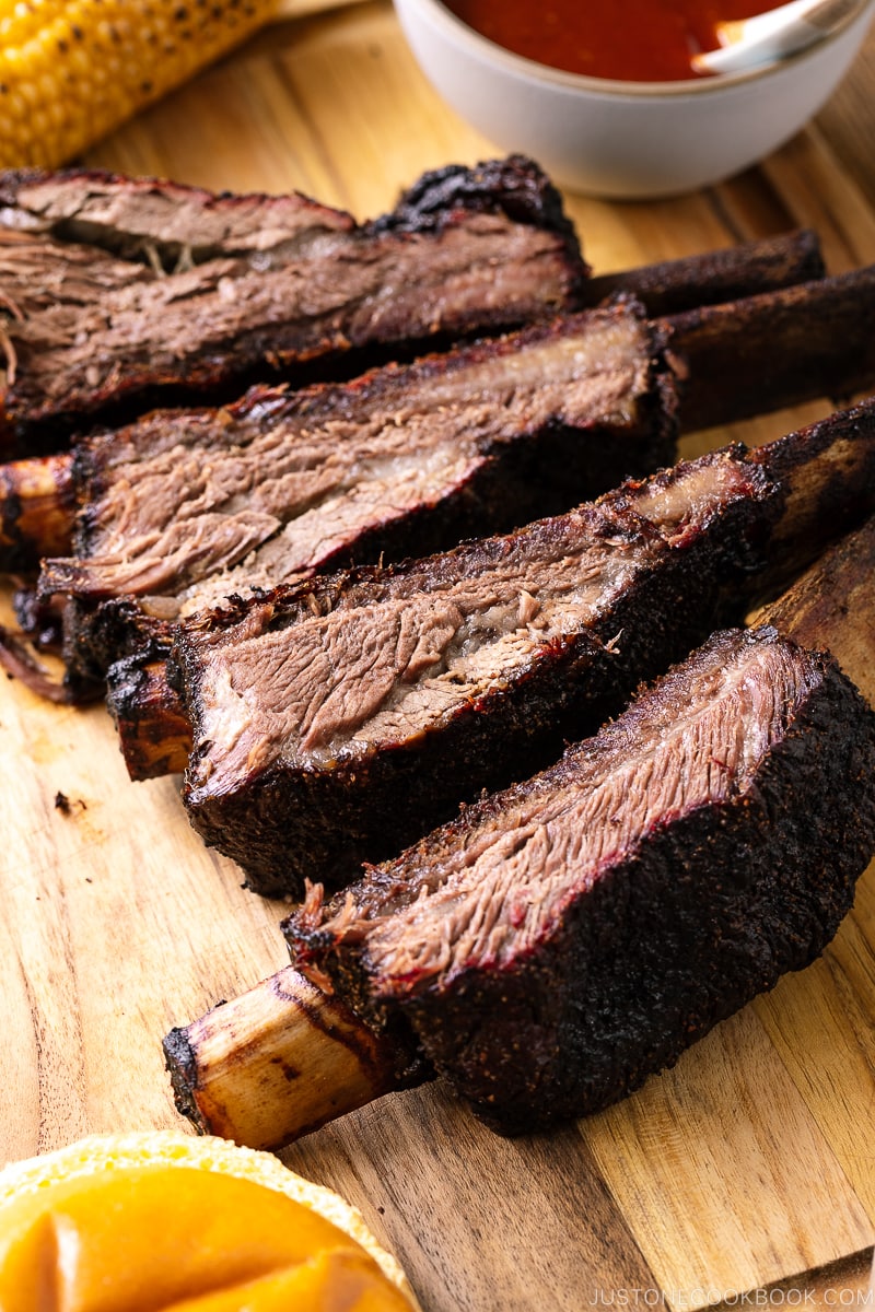 A baking sheet containing smoked beef ribs and bbq sauce.