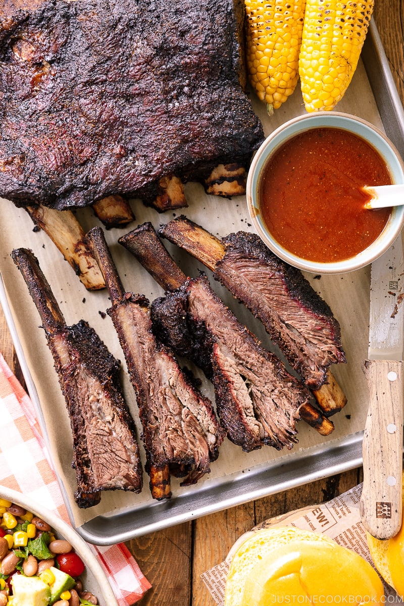 A baking sheet containing smoked beef ribs and bbq sauce.