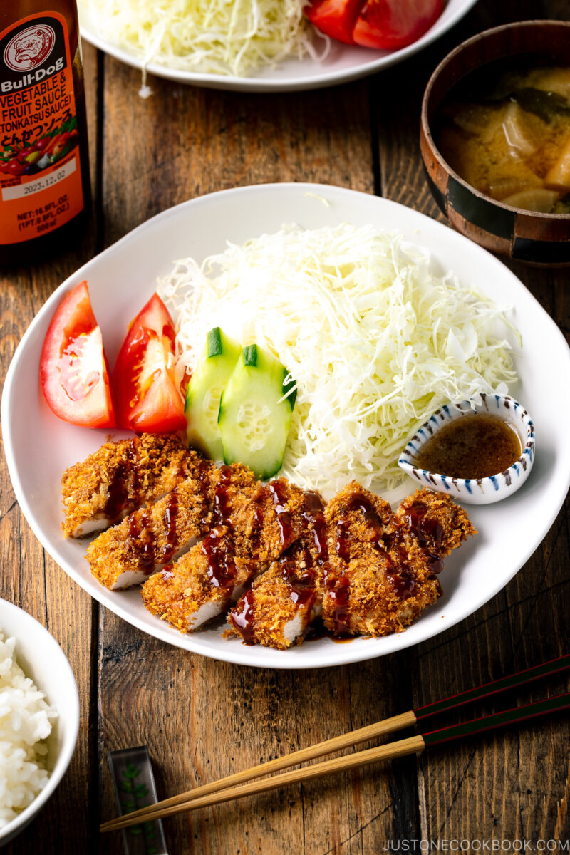 A white plate containing Baked Chicken Katsu (Japanese Chicken Cutlets) and shredded cabbage salad.