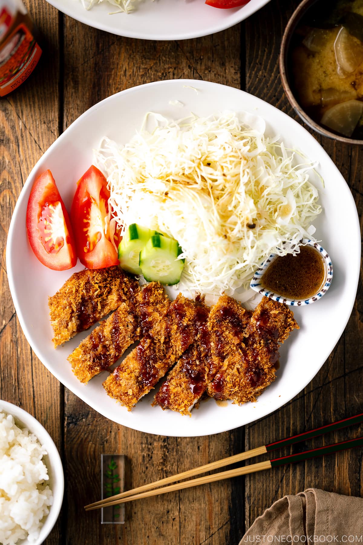 A white plate containing Baked Chicken Katsu (Japanese Chicken Cutlets) and shredded cabbage salad.