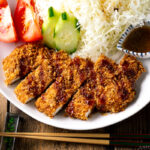 A white plate containing Baked Chicken Katsu (Japanese Chicken Cutlets) and shredded cabbage salad.