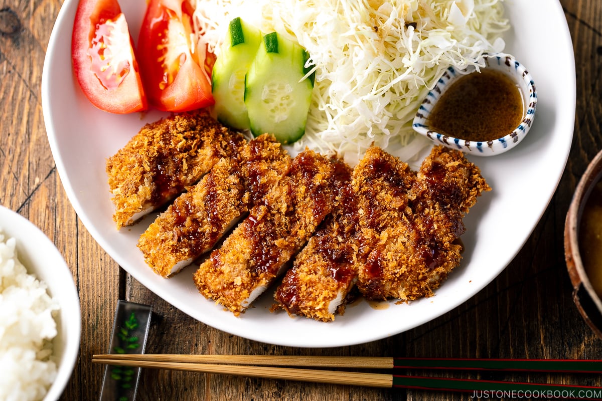 A white plate containing Baked Chicken Katsu (Japanese Chicken Cutlets) and shredded cabbage salad.