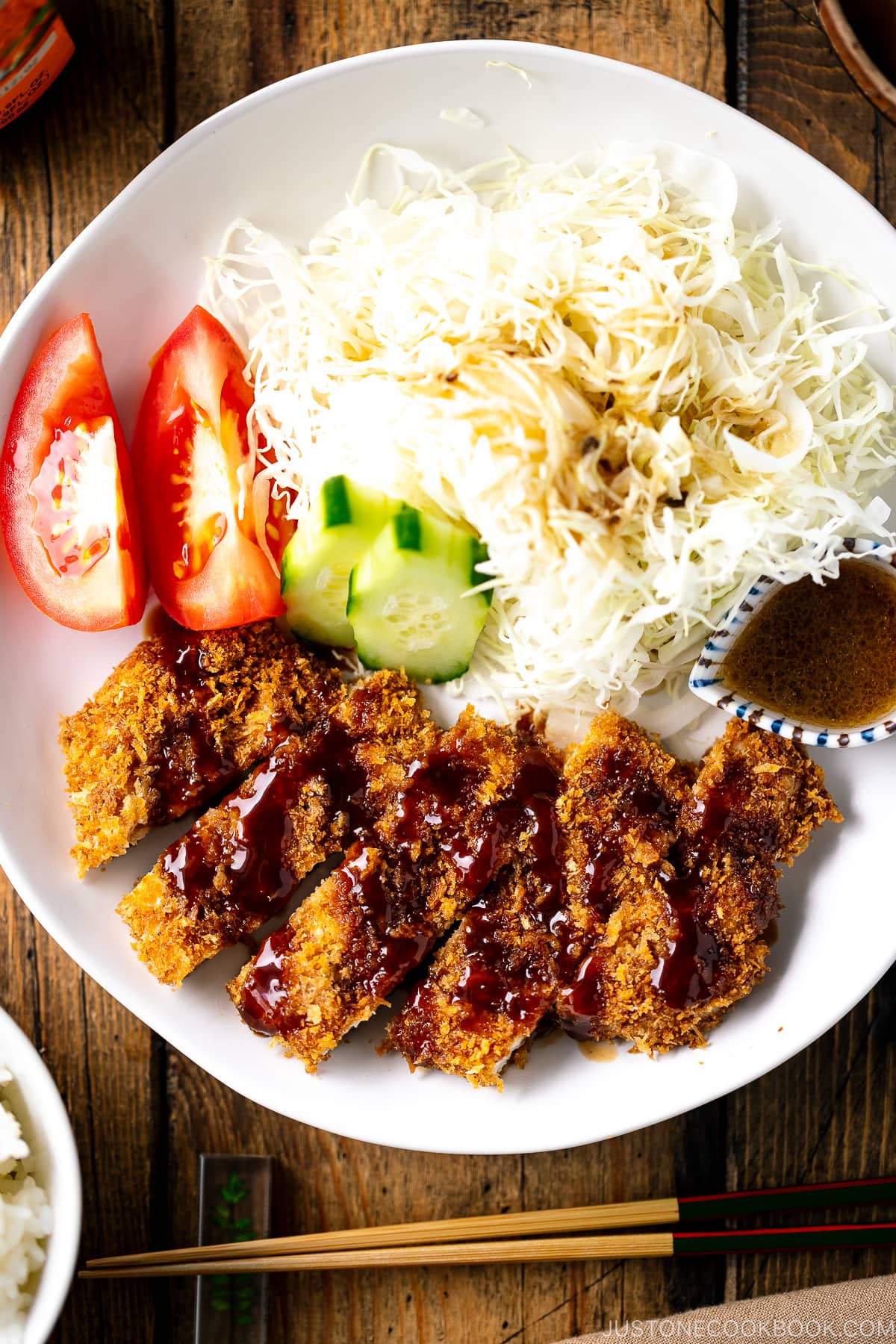 A white plate containing Baked Chicken Katsu (Japanese Chicken Cutlets), shredded cabbage salad, and tomato slices.