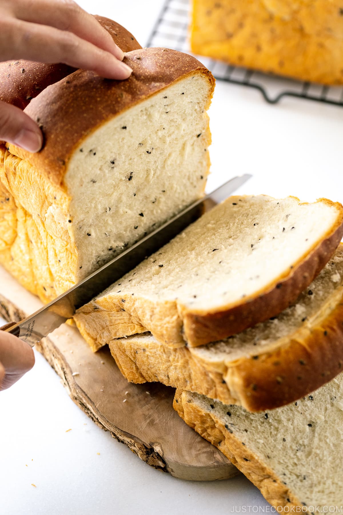 Slicing a loaf of Black Sesame Shokupan (Japanese Milk Bread) with a bread knife.