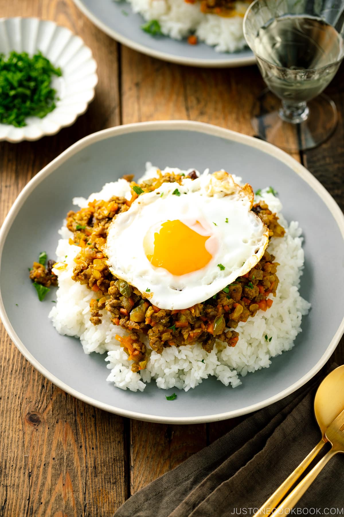 A ceramic plate containing steamed rice, dry curry, and a fried egg.