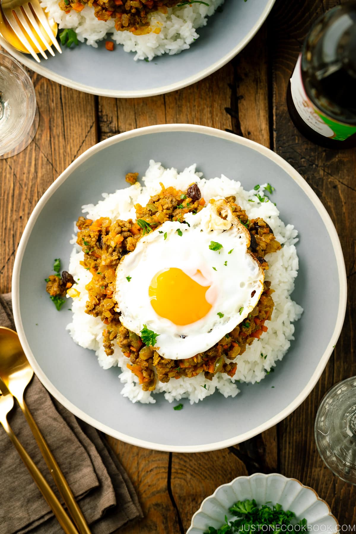 Un piatto di ceramica contenente riso al vapore, curry secco e un uovo fritto.