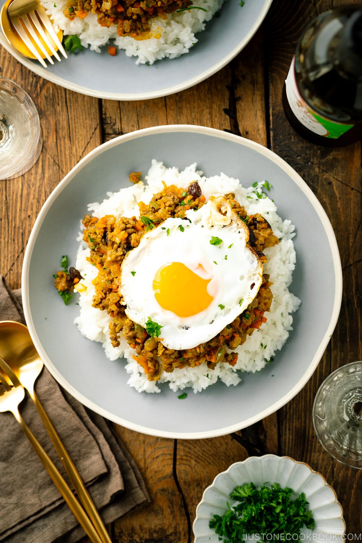 Un piatto di ceramica contenente riso al vapore, curry secco e un uovo fritto.