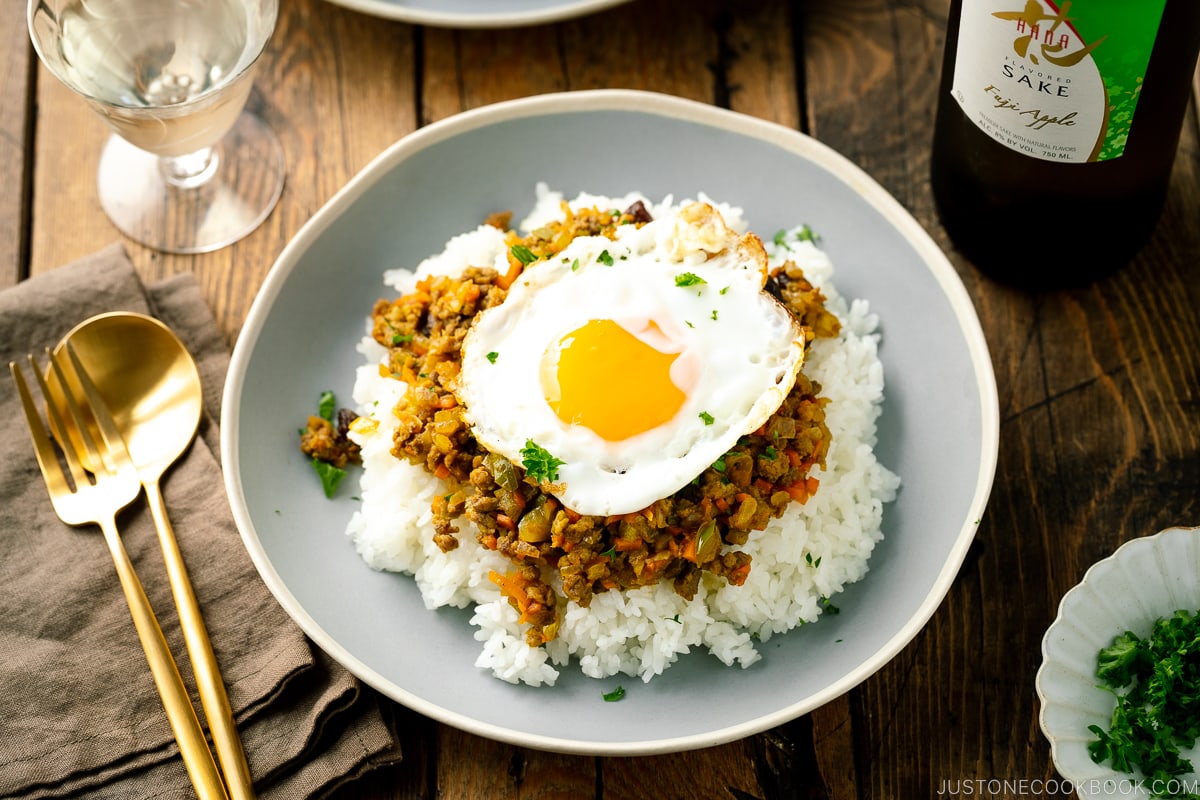 A ceramic plate containing steamed rice, dry curry, and a fried egg.