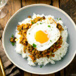 A ceramic plate containing steamed rice, dry curry, and a fried egg.