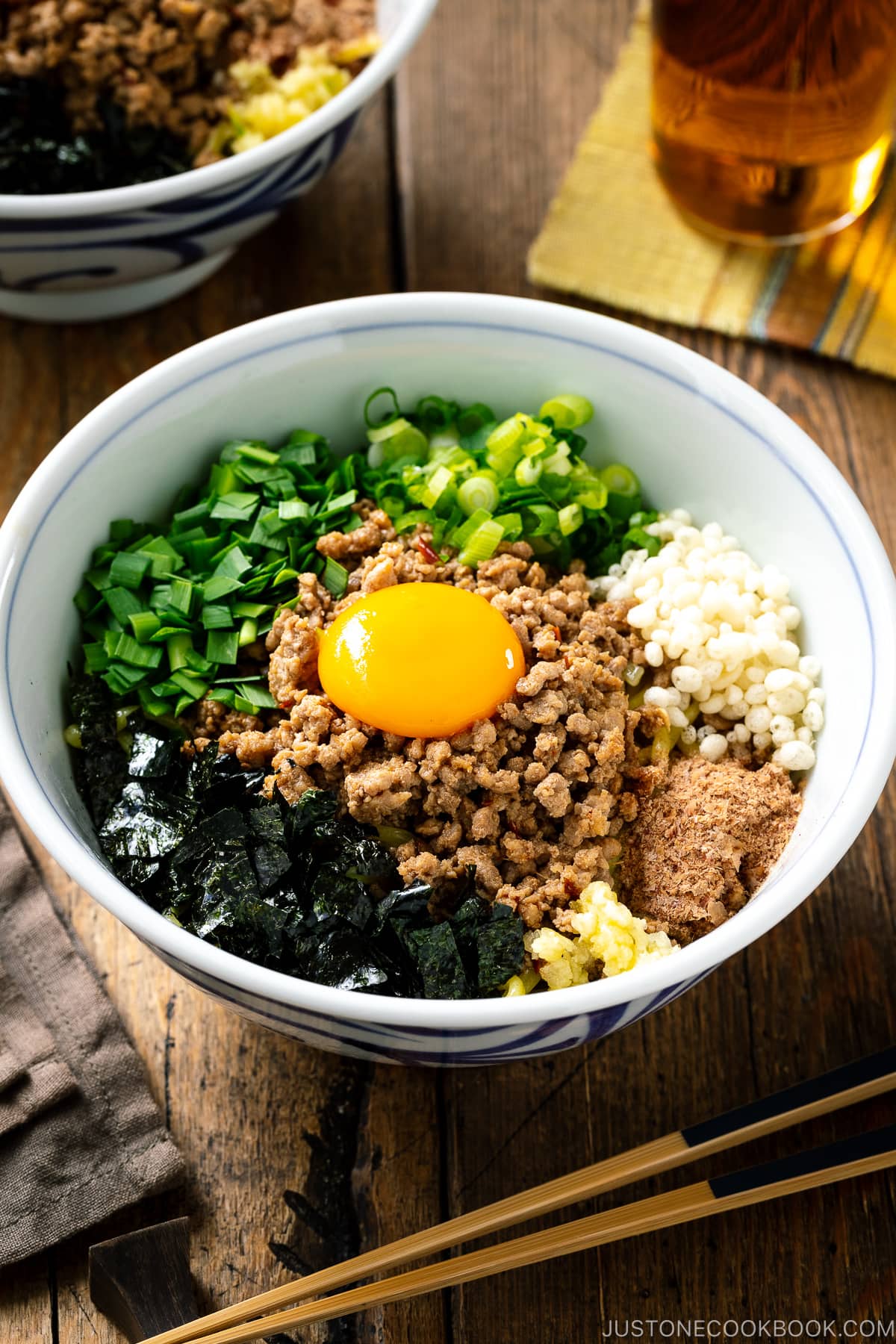 A bowl containing Mazesoba (Mazemen), Japanese Brothless Ramen, topped with seasoned minced meat, green onion, garlic chives, nori seaweed, crushed garlic, and katsuobushi powder.