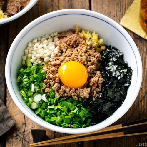 A bowl containing Mazesoba (Mazemen), Japanese Brothless Ramen, topped with seasoned minced meat, green onion, garlic chives, nori seaweed, crushed garlic, and katsuobushi powder.