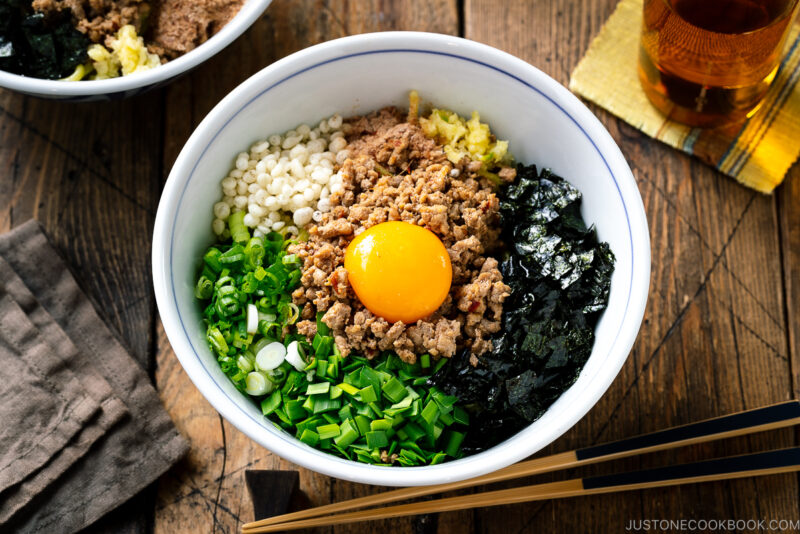 A bowl containing Mazesoba (Mazemen), Japanese Brothless Ramen, topped with seasoned minced meat, green onion, garlic chives, nori seaweed, crushed garlic, and katsuobushi powder.