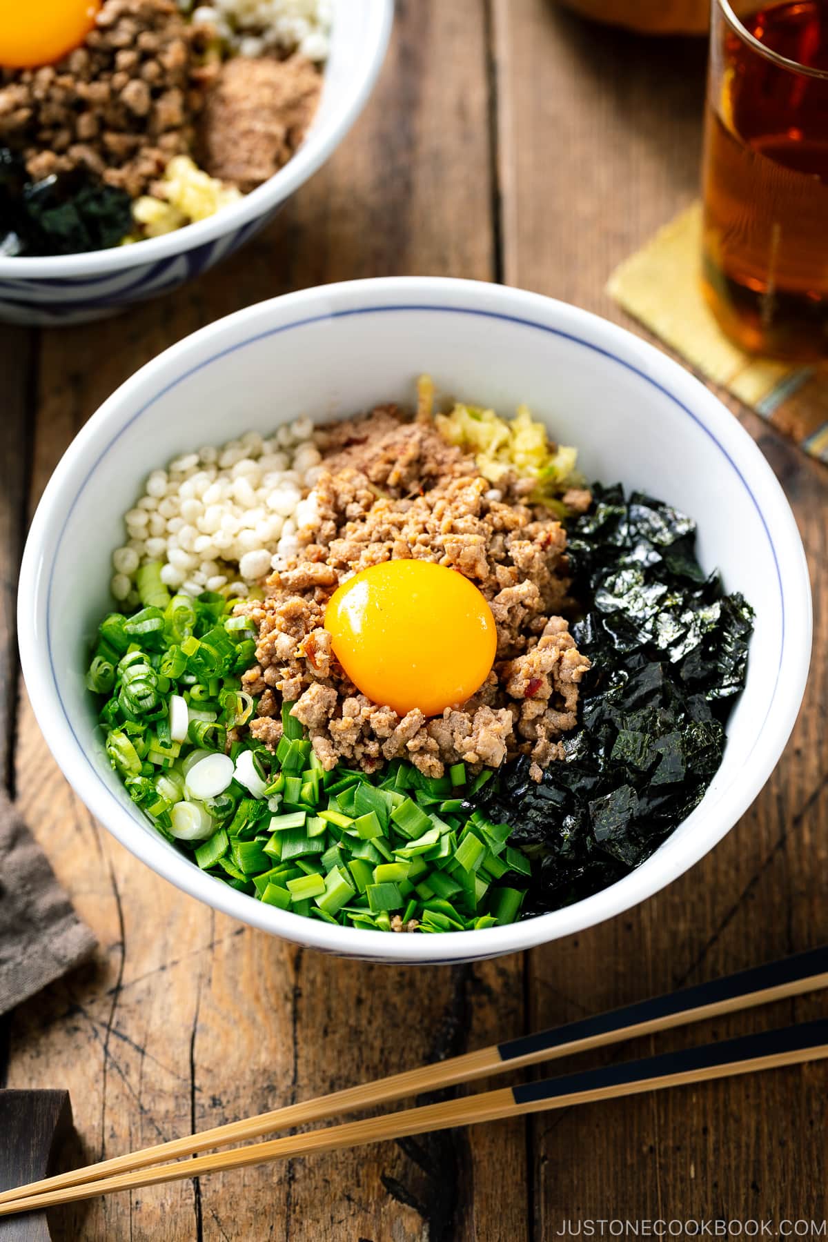 A bowl containing Mazesoba (Mazemen), Japanese Brothless Ramen, topped with seasoned minced meat, green onion, garlic chives, nori seaweed, crushed garlic, and katsuobushi powder.