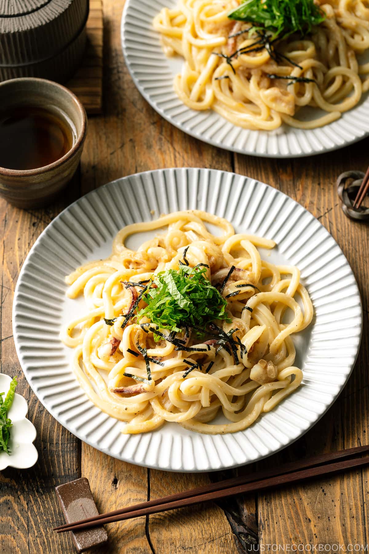 A white plate containing Mentaiko Udon topped with shredded nori and shiso leaves.