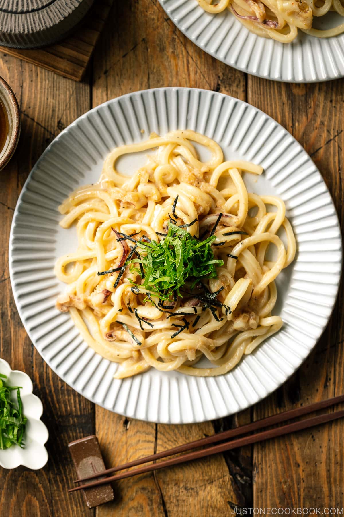 A white plate containing Mentaiko Udon topped with shredded nori and shiso leaves.