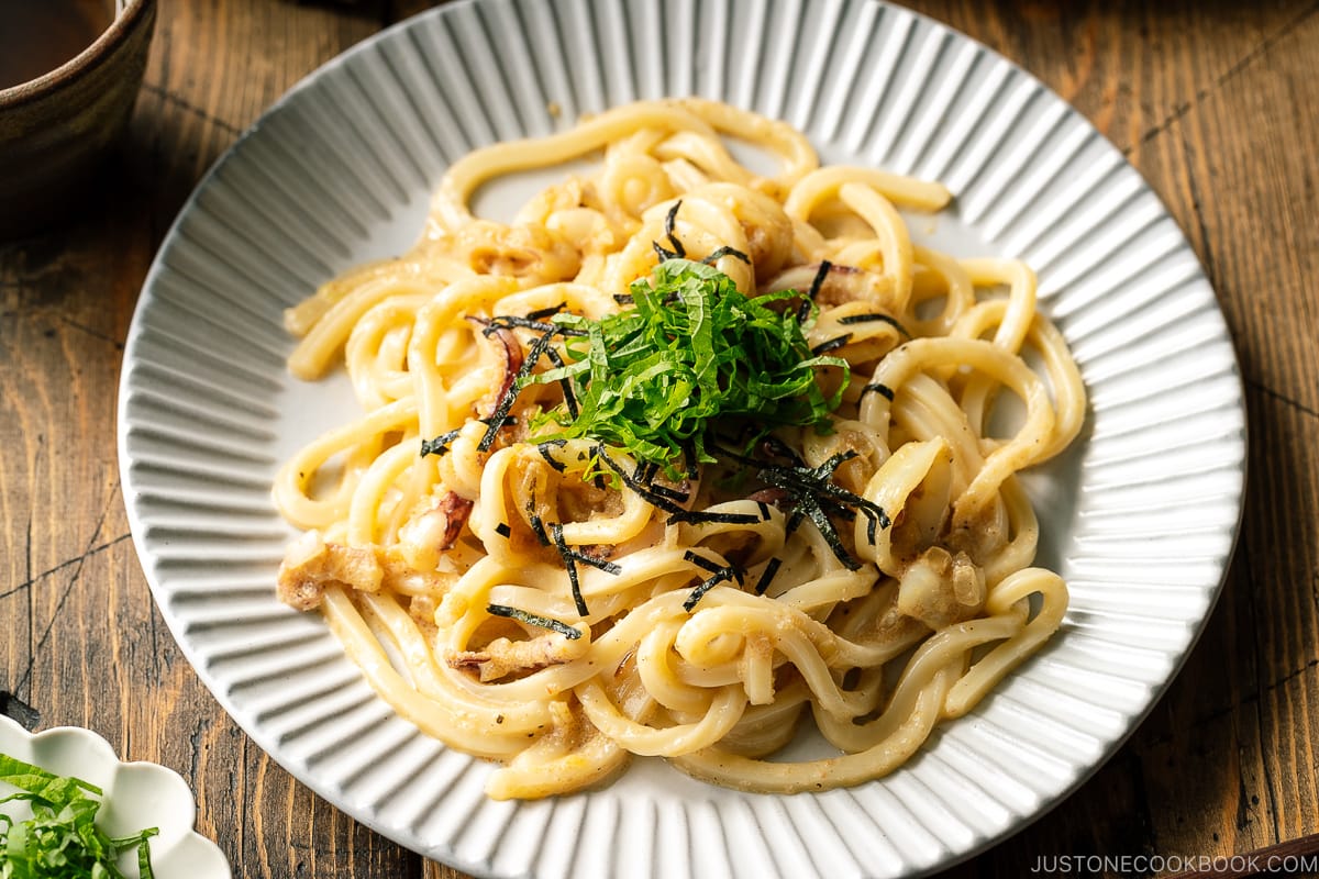A white plate containing Mentaiko Udon topped with shredded nori and shiso leaves.