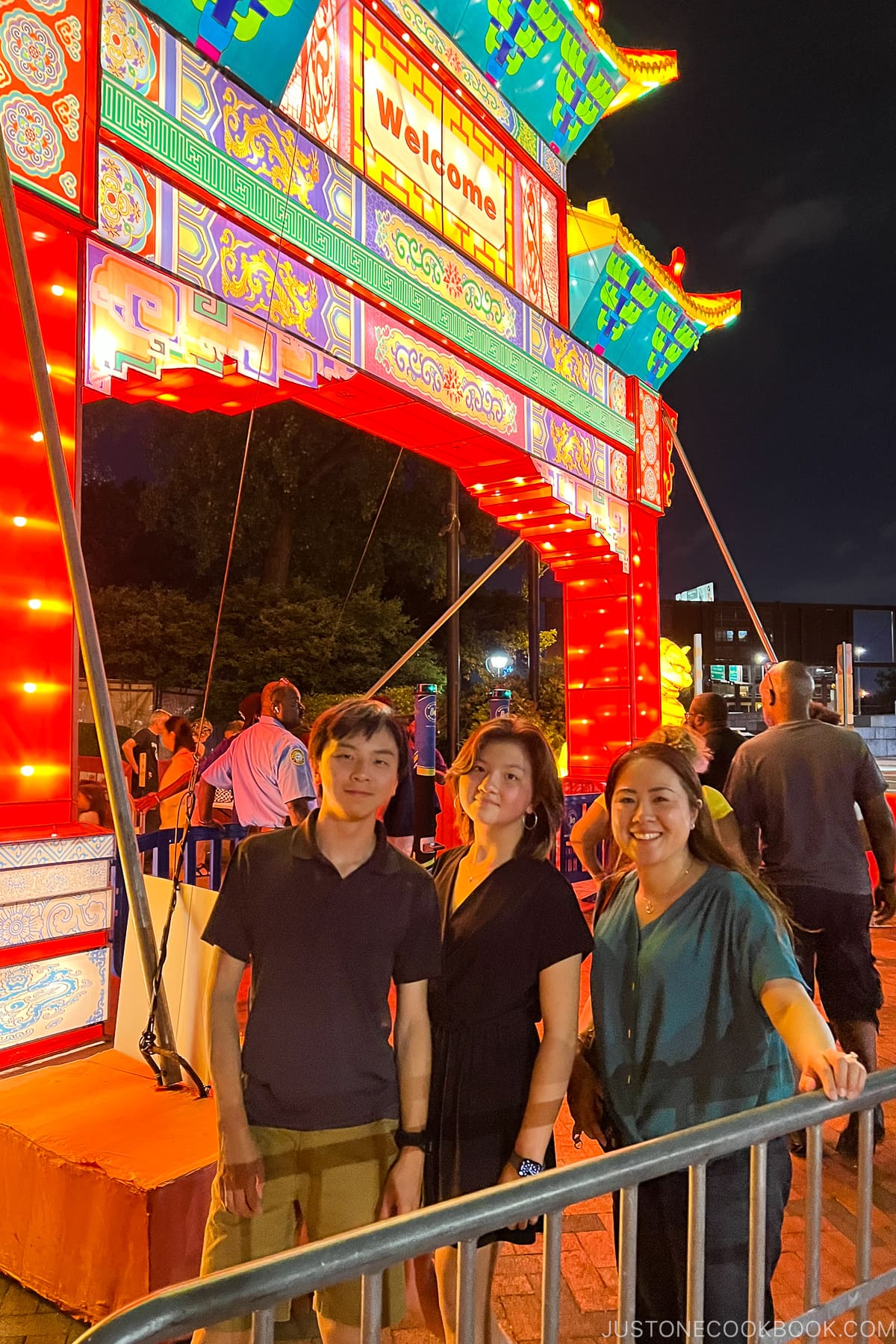 three people standing next to a lit lantern gate