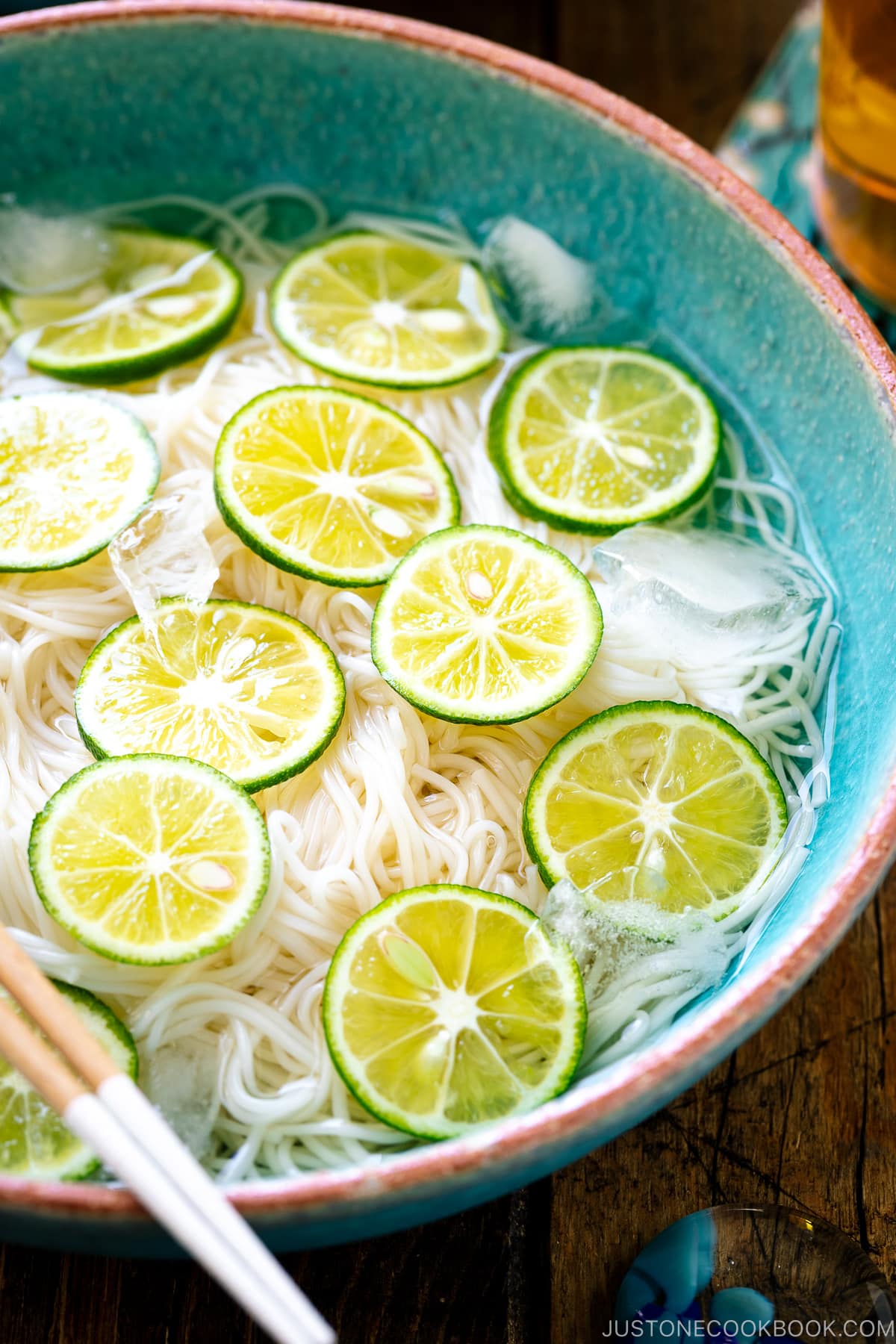 A blue bowl containing cold somen noodles topped with thinly sliced sudachi citrus.