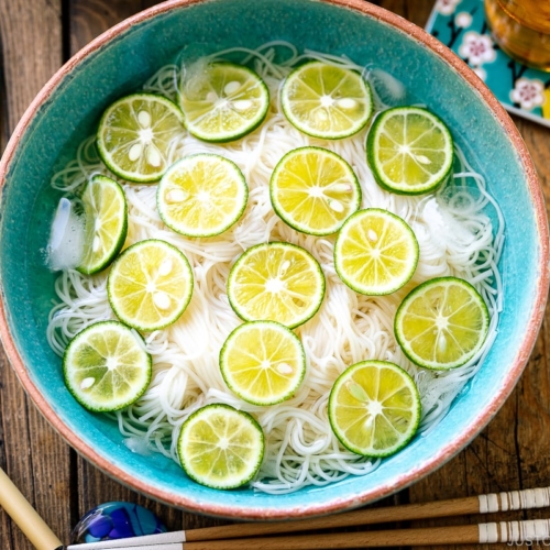 A blue bowl containing cold somen noodles topped with thinly sliced sudachi citrus.