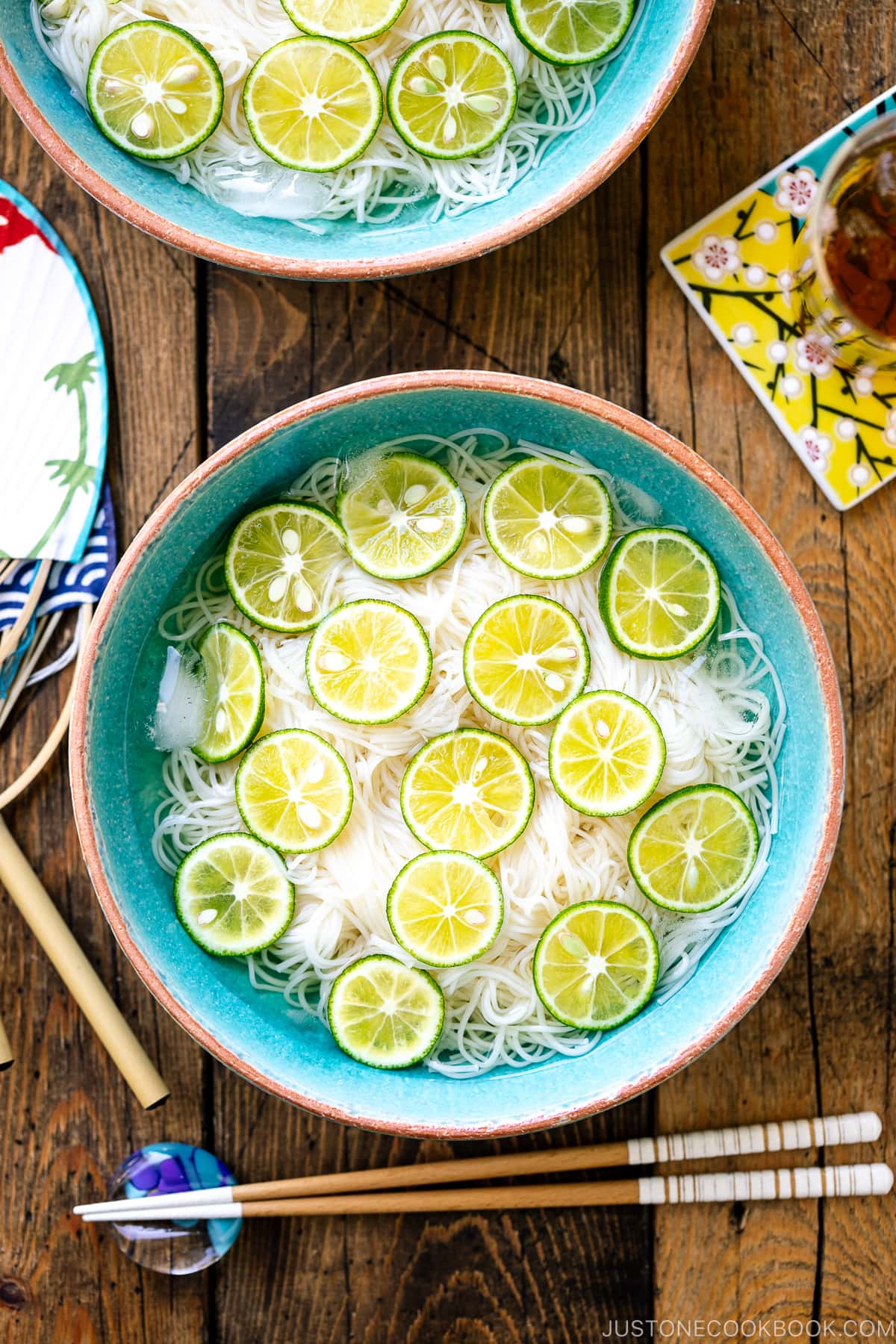 A blue bowl containing cold somen noodles topped with thinly sliced sudachi citrus.