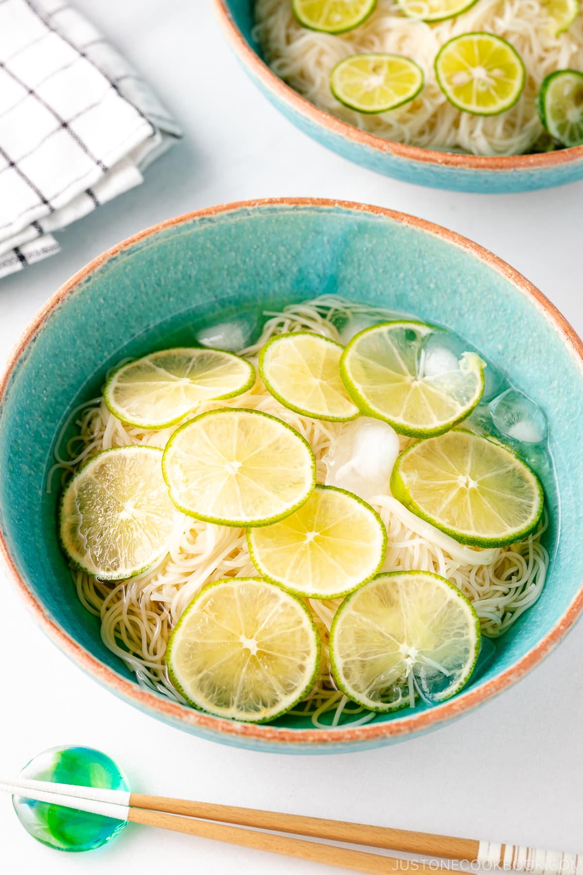 A blue bowl containing cold somen noodles topped with thinly sliced lime.