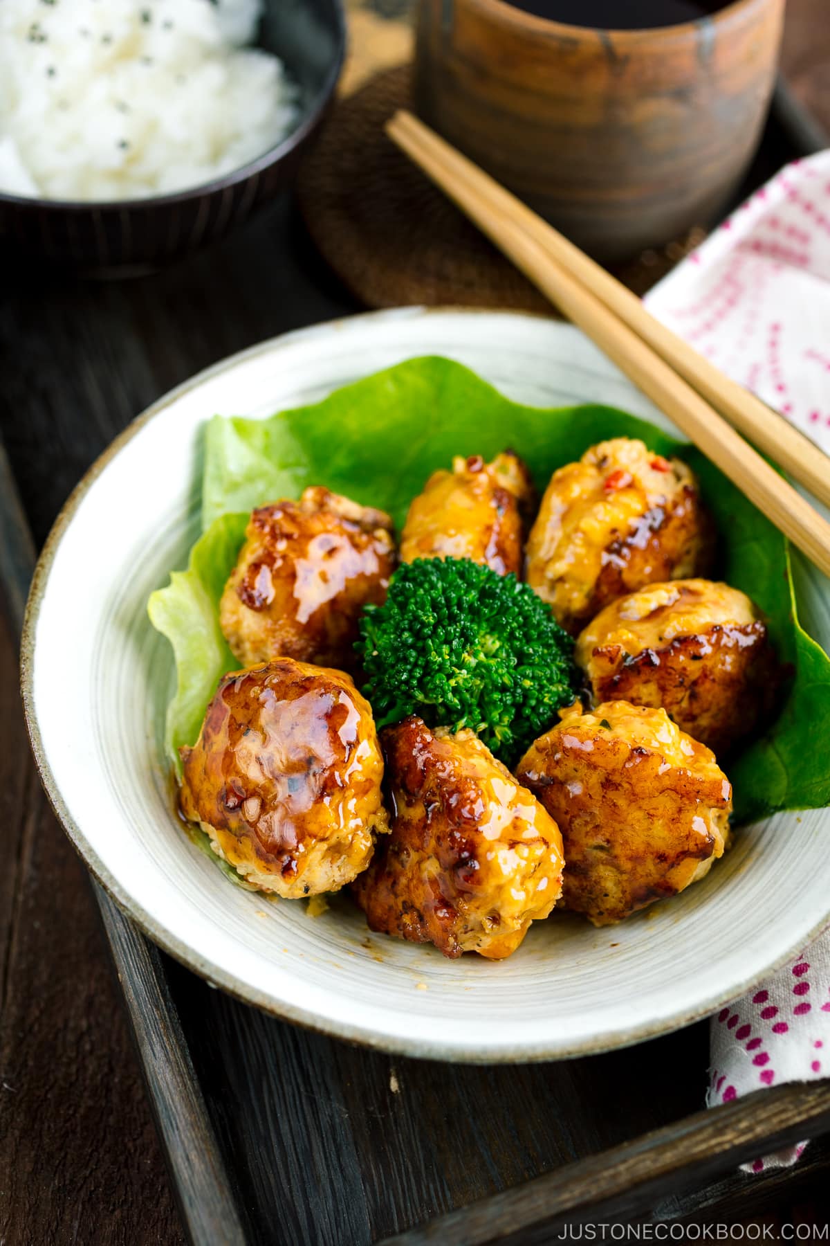 A white bowl containing teriyaki chicken meatballs and broccoli.