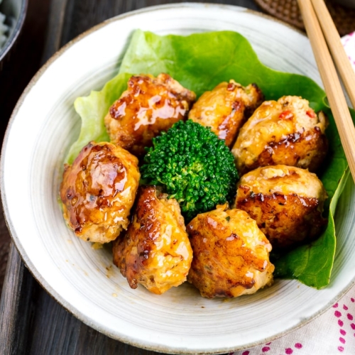 A white bowl containing teriyaki chicken meatballs and broccoli.