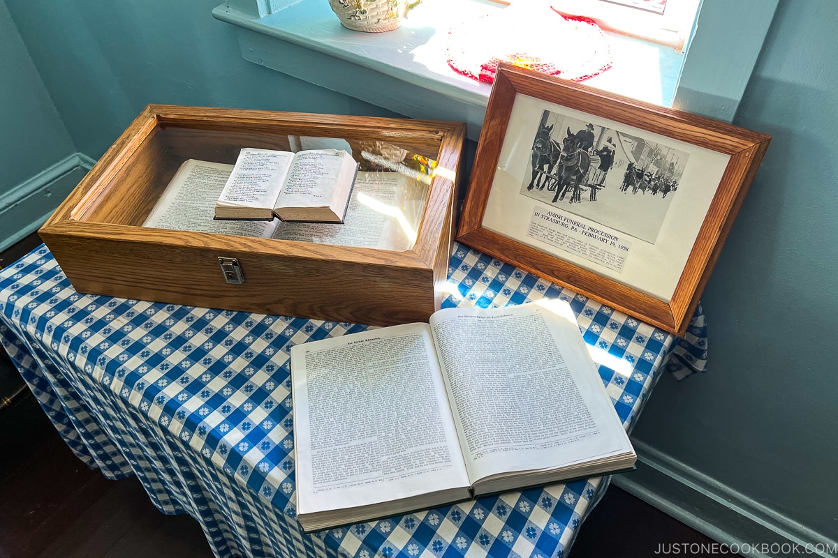 a book in a glass display case next to a book on a table with blue and white table cloth