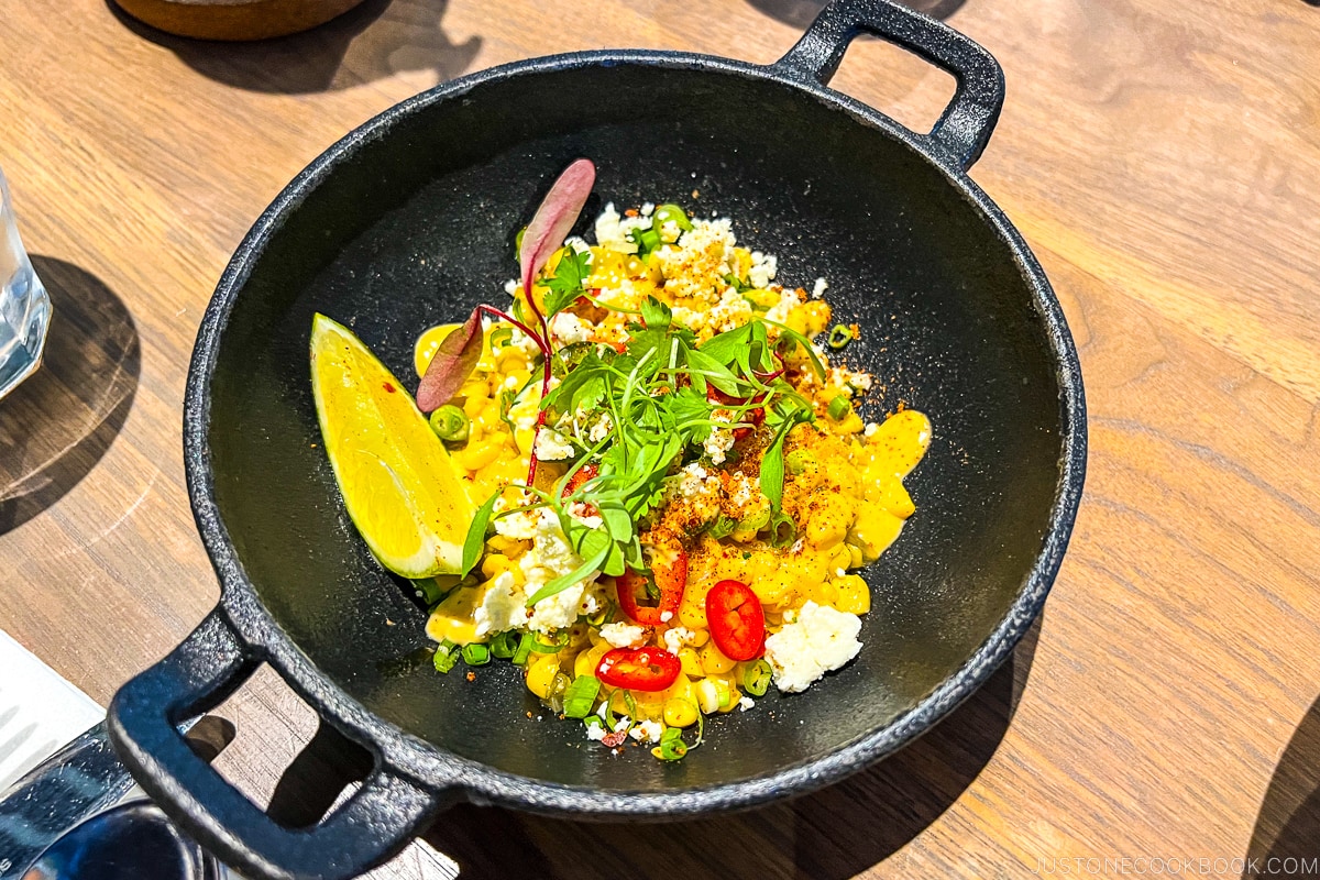 Roasted yellow corn, cotija cheese, chili lime powder, spicy aioli in a black bowl