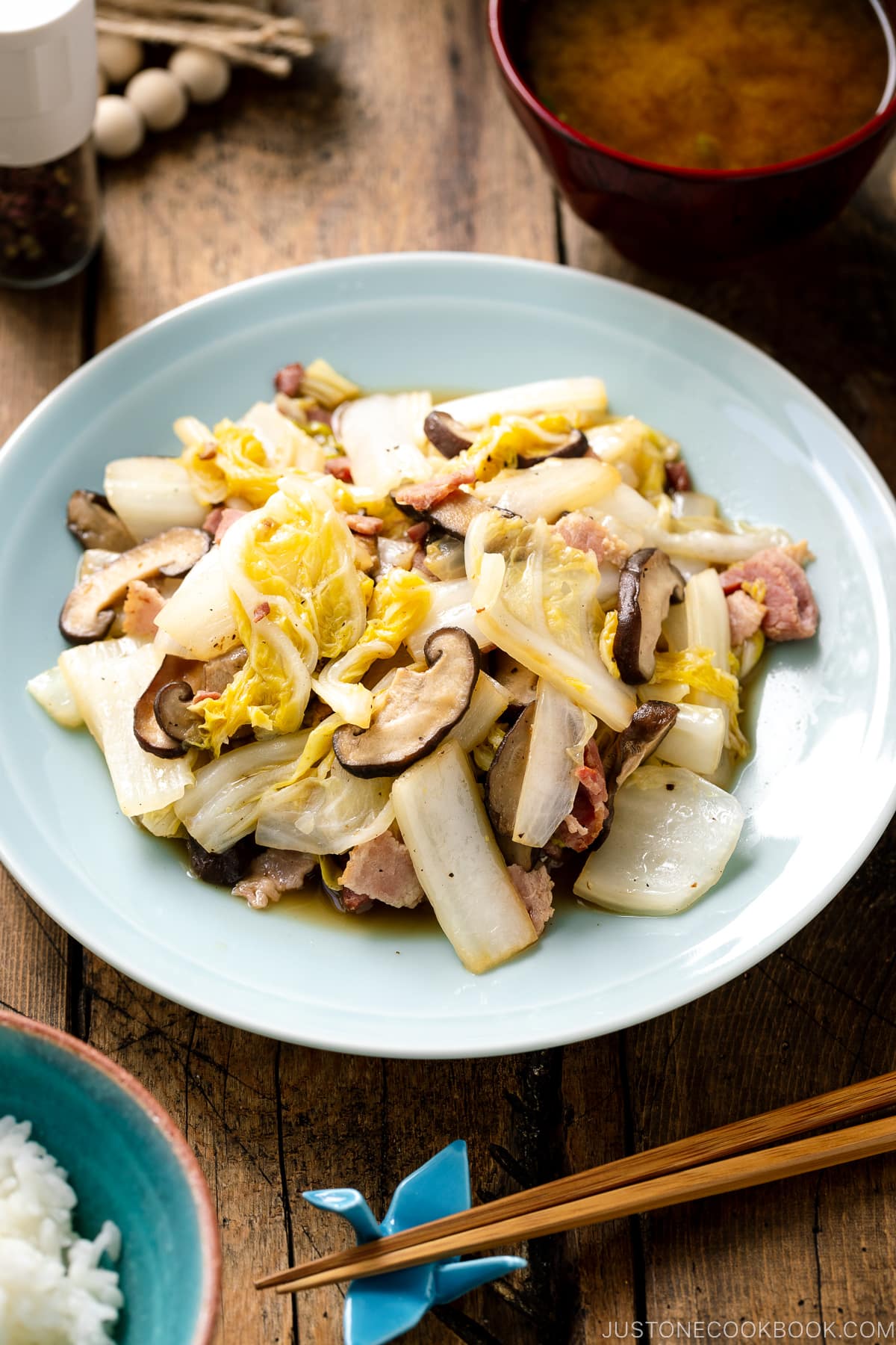 A round ceramic plate containing napa cabbage stir-fry with shiitake mushrooms and bacon seasoned lightly with soy sauce.