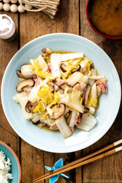 A round ceramic plate containing napa cabbage stir-fry with shiitake mushrooms and bacon seasoned lightly with soy sauce.