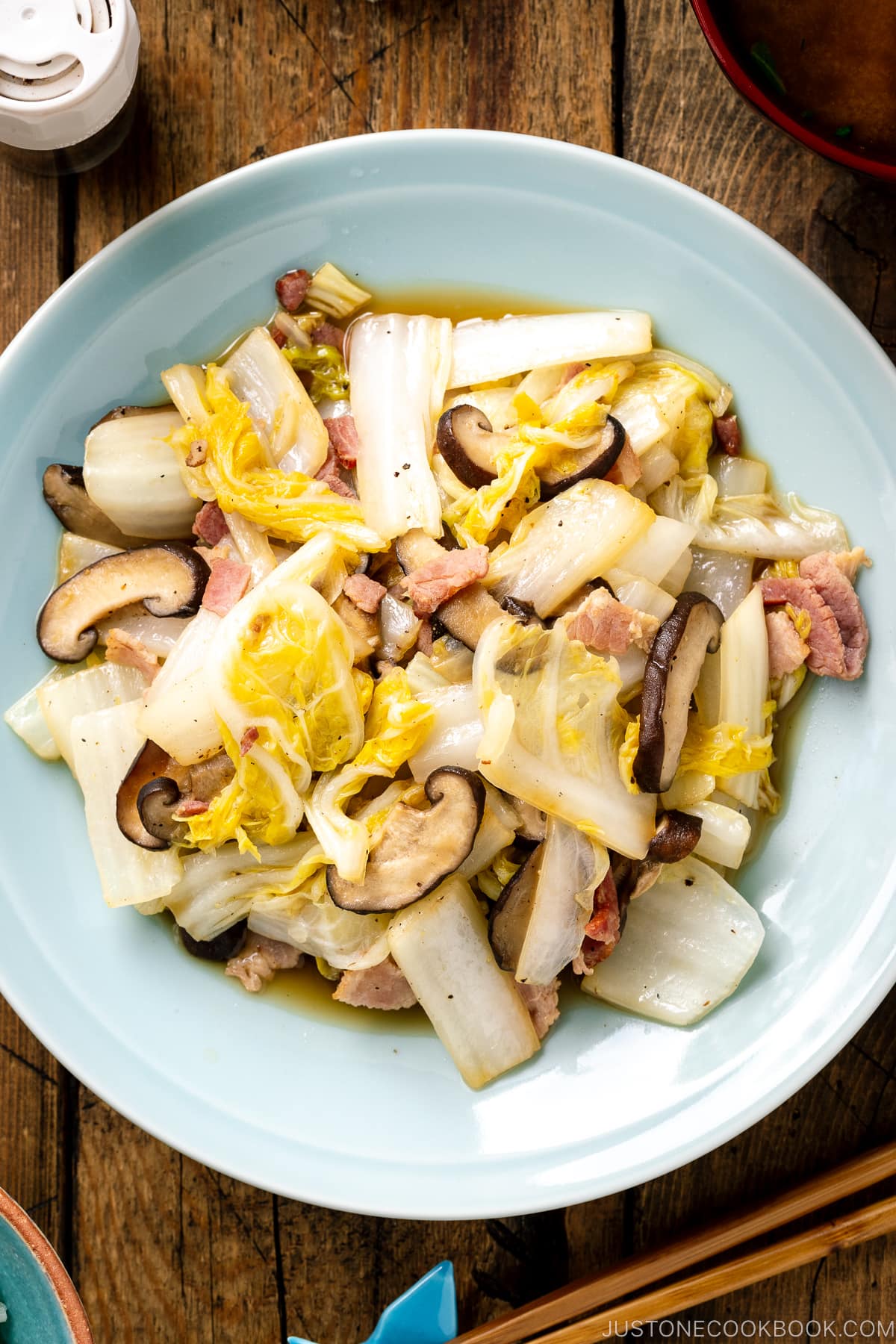 A round ceramic plate containing napa cabbage stir-fry with shiitake mushrooms and bacon seasoned lightly with soy sauce.