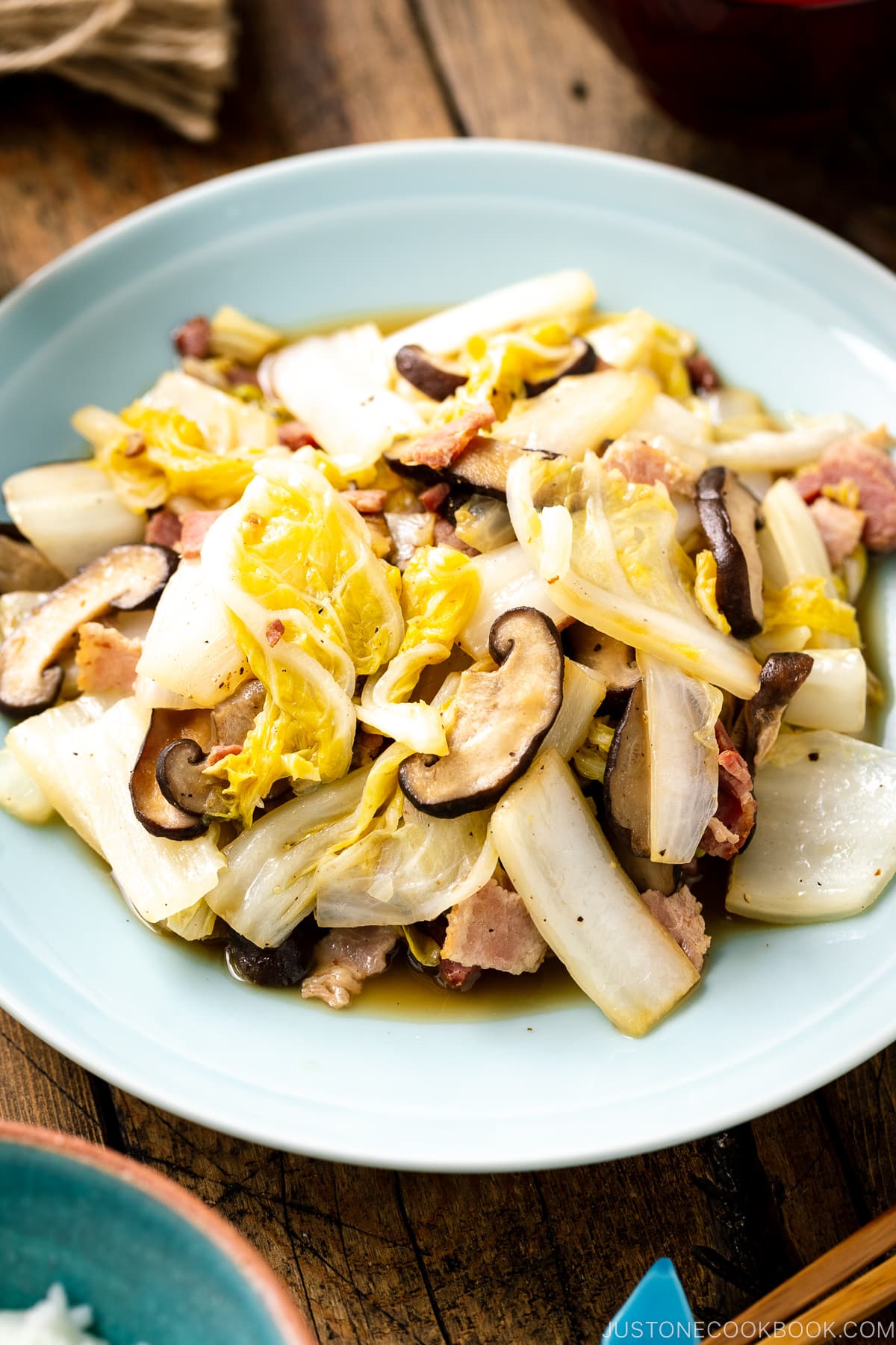 A round ceramic plate containing napa cabbage stir-fry with shiitake mushrooms and bacon seasoned lightly with soy sauce.