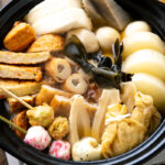 A donabe clay pot containing Japanese fish cake stew called oden, an assortment of fish balls and fish cakes.