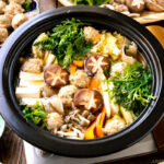 A Japanese clay pot simmering chicken meatballs, tofu, mushrooms, and various vegetables in a savory dashi broth.