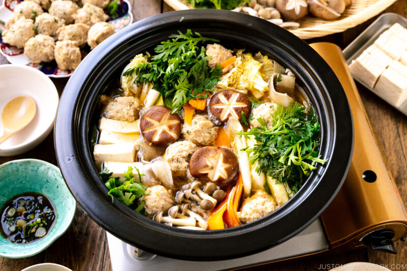 A Japanese clay pot simmering chicken meatballs, tofu, mushrooms, and various vegetables in a savory dashi broth.
