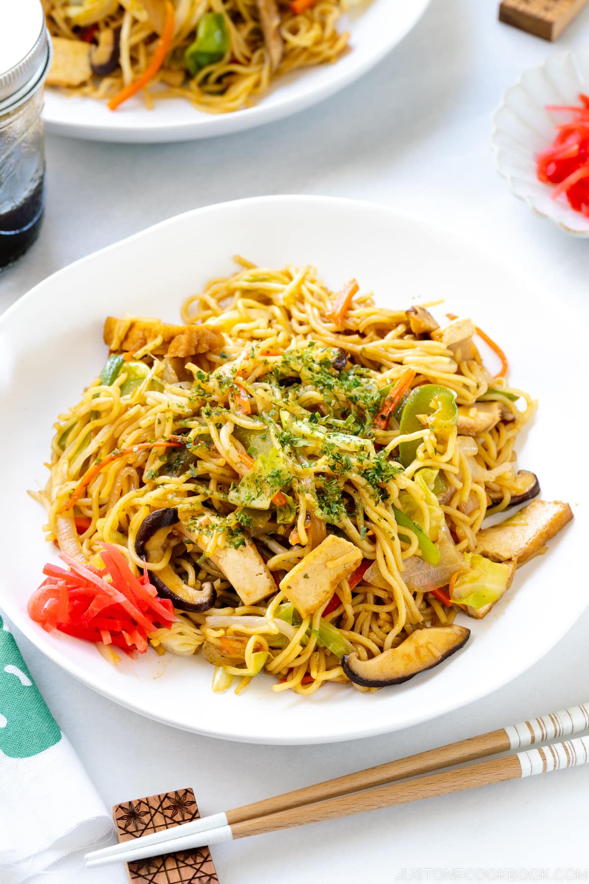 A white plate containing vegetable yakisoba along with red pickled ginger.