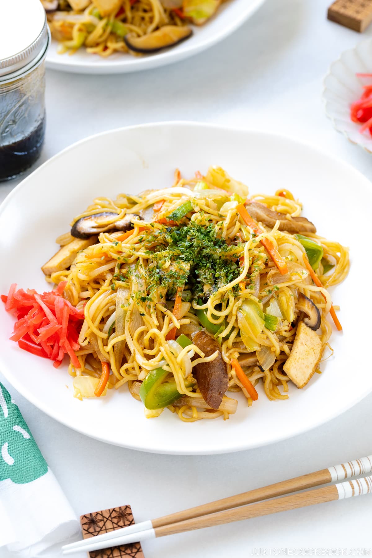 A white plate containing vegetable yakisoba along with red pickled ginger.