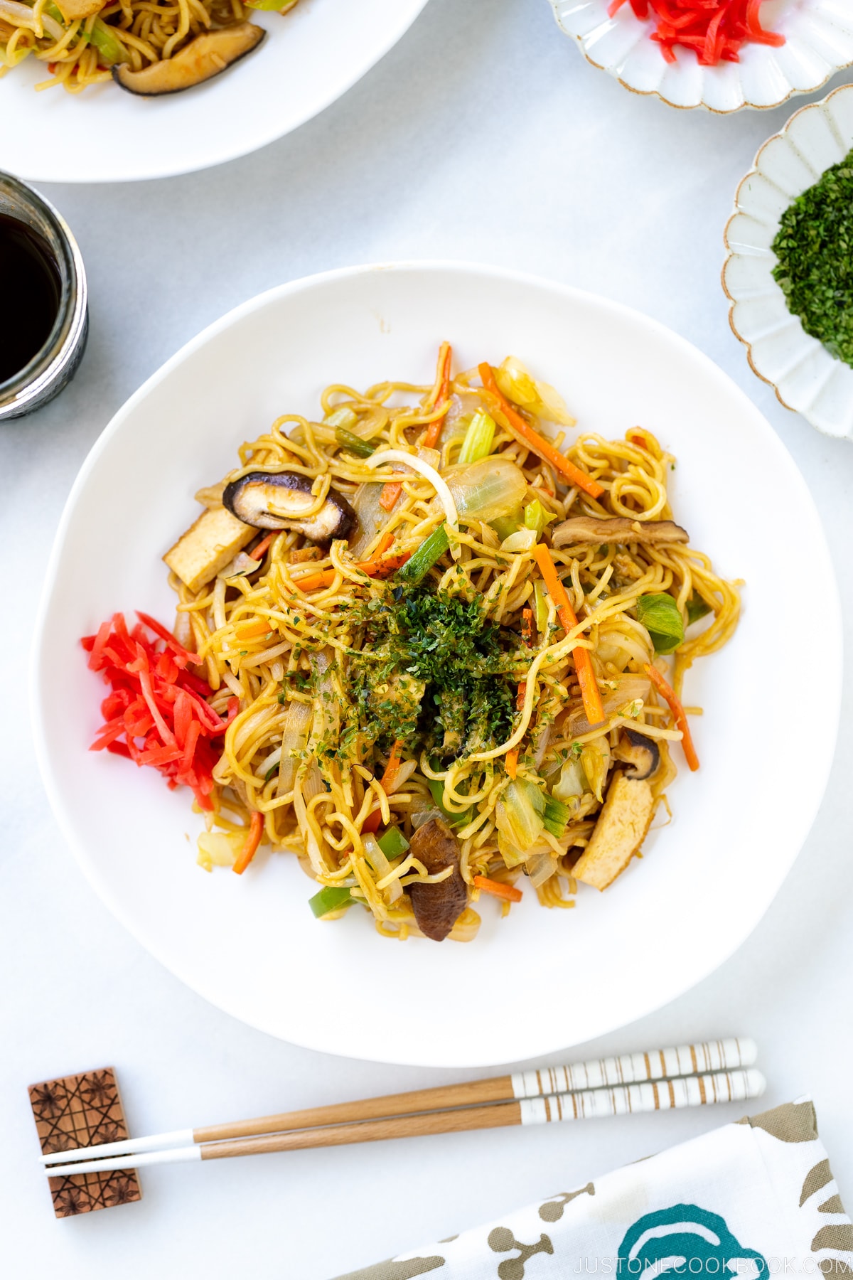 A white plate containing vegetable yakisoba along with red pickled ginger.