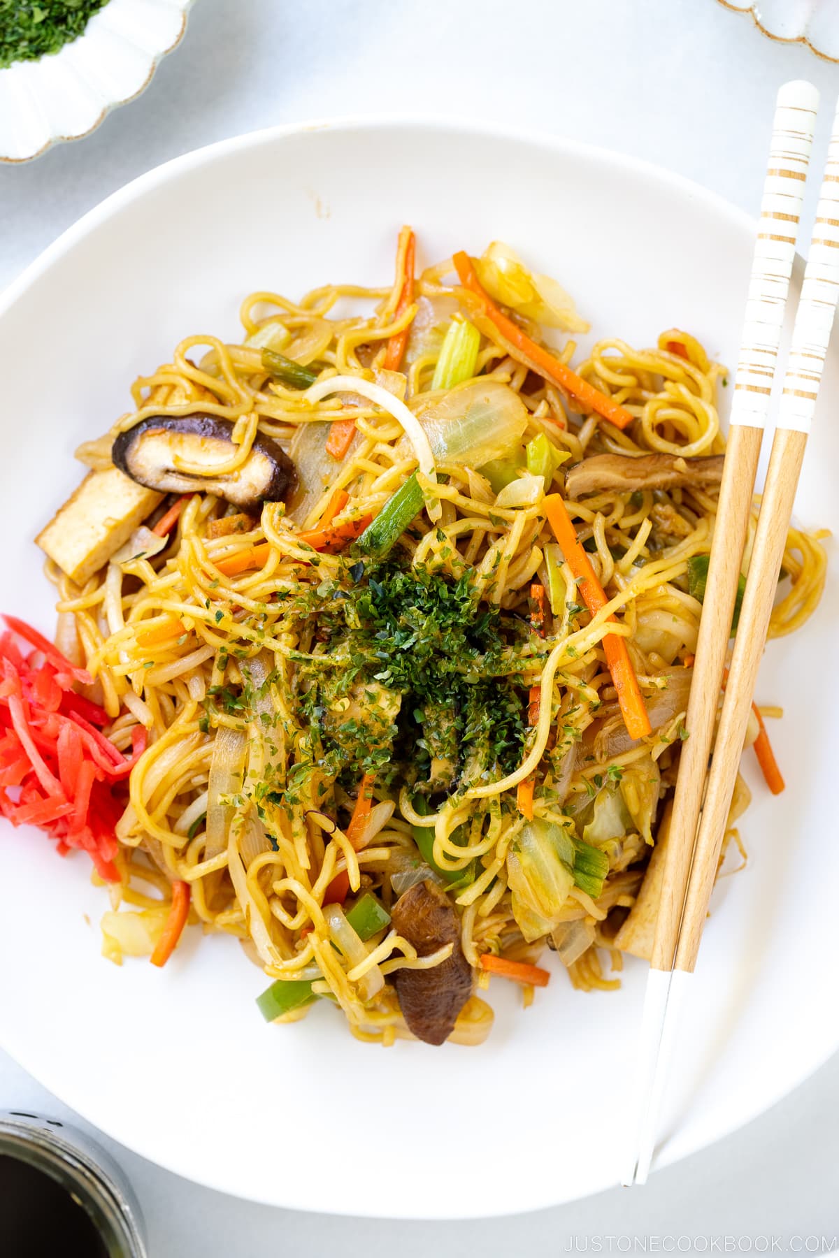 A white plate containing vegetable yakisoba along with red pickled ginger.