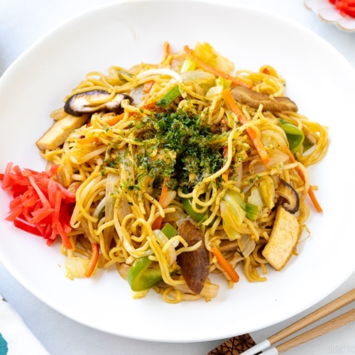 A white plate containing vegetable yakisoba along with red pickled ginger.