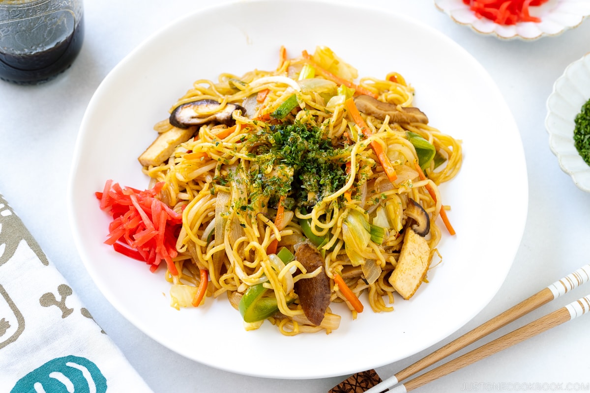 A white plate containing vegetable yakisoba along with red pickled ginger.