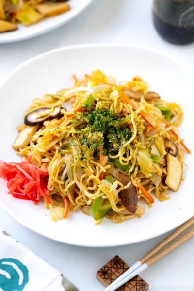 A white plate containing vegetable yakisoba along with red pickled ginger.