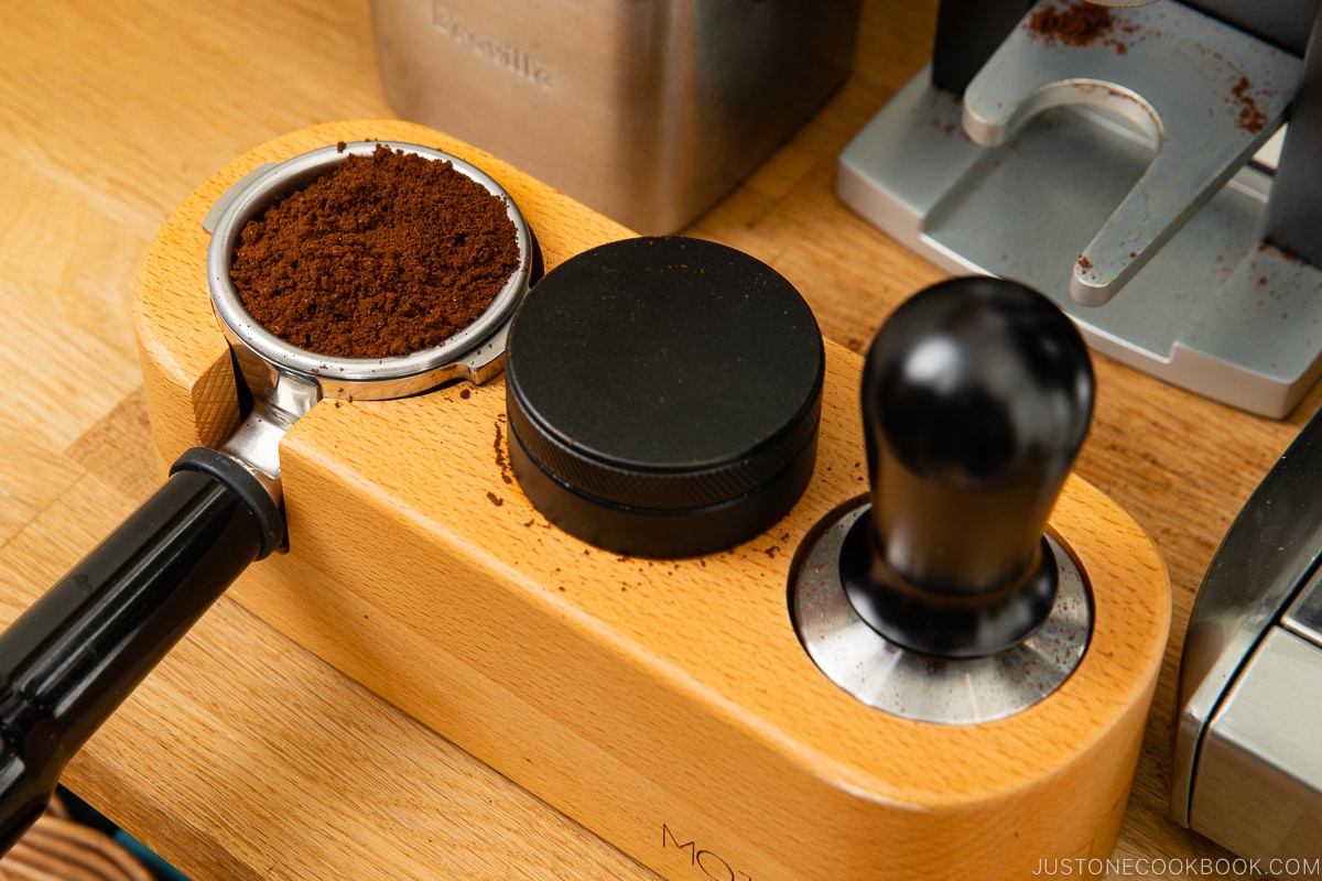 ground coffee in a portafilter next to a distributor and tamper