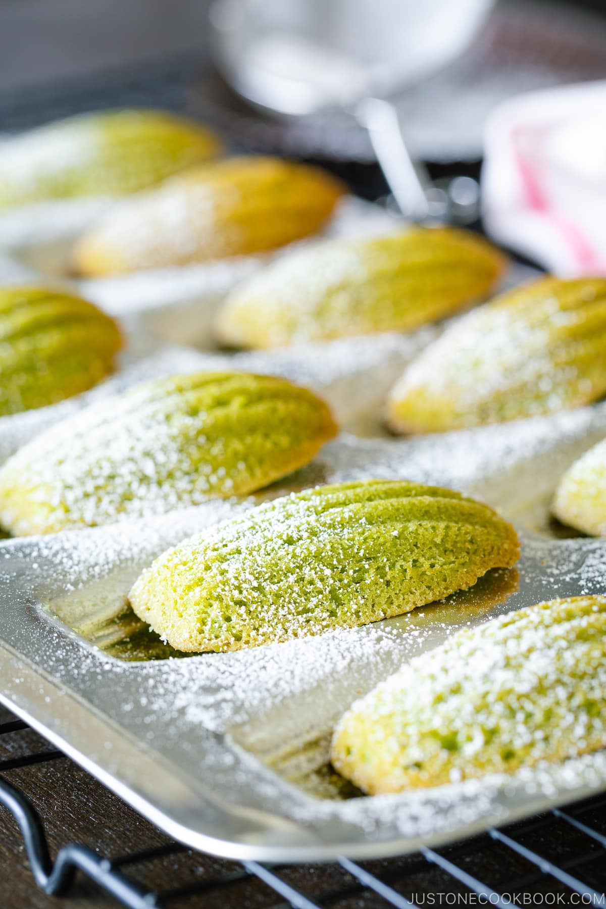 A Madeleine pan containing matcha green tea madeleines dusted with powdered sugar.