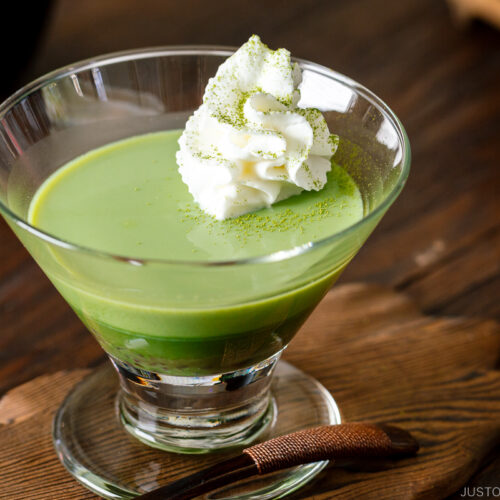 A glass containing matcha pudding with whipped cream.